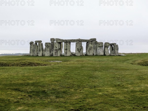 Distant view of Stonehenge surrounded by green grass under an overcast sky. Salisbury, England, United Kingdom