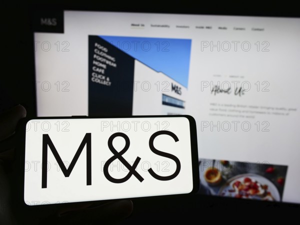 Stuttgart, Germany, 03-18-2024: Person holding smartphone with logo of British retail company Marks and Spencer Group plc in front of website. Focus on phone display