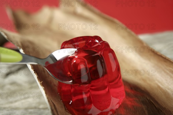 Jelly in red strawberry color in green spoon over wood