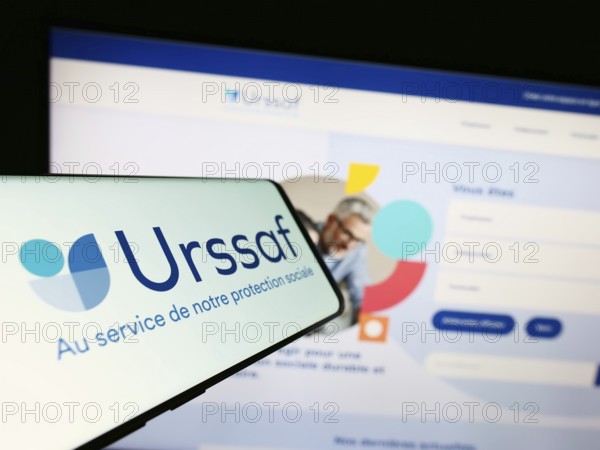 Stuttgart, Germany, 07-12-2023: Smartphone with logo of French social security organization URSSAF on screen in front of website. Focus on center-left of phone display