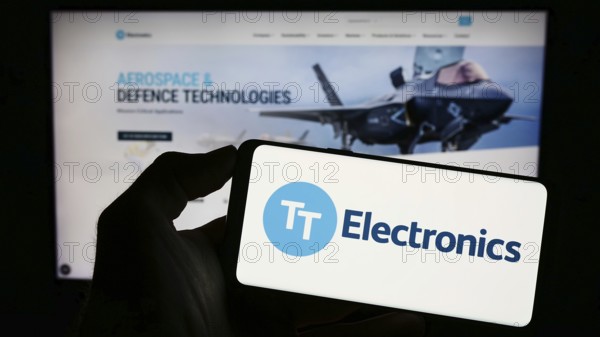 Stuttgart, Germany, 04-20-2023: Person holding cellphone with logo of British company TT Electronics plc on screen in front of business webpage. Focus on phone display