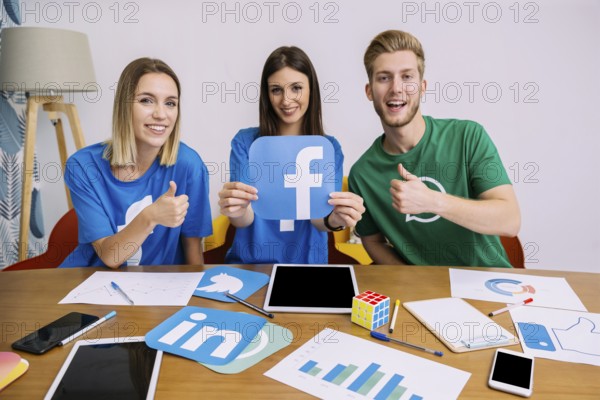 Smiling woman holding facebook logo with his friends showing thumbup sign