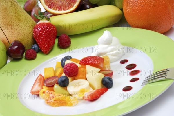Fruit salad with cream arranged on a plate in front of fresh fruit