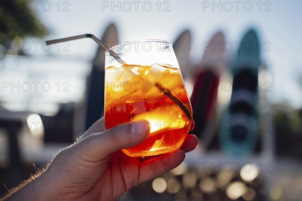 Orange slice and aperol spritz cocktail on a stone against the backdrop of a sandy beach. Man holding slass with iced citrus sparkling mineral water and straw. Copy space