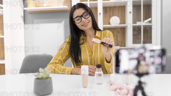 Female vlogger home with smartphone make up products