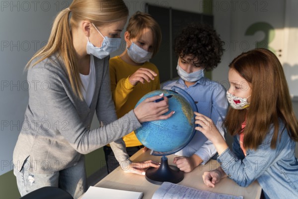 Female teacher with medical mask teaching geography with earth globe class