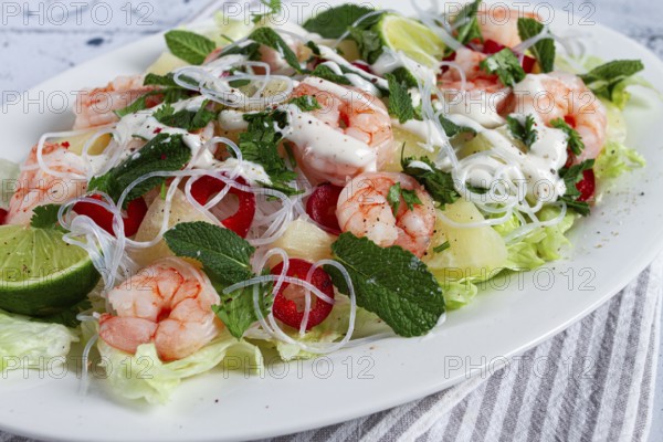 Thai salad with shrimp and rice noodles, pineapple slices, coriander and mint leaves, on a white plate, homemade, no people