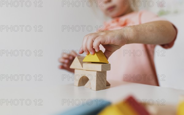 Little child girl playing wooden building blocks at home or kindergarten. Development and construction concept. Multi-colored educational bricks for early learning and education for young children