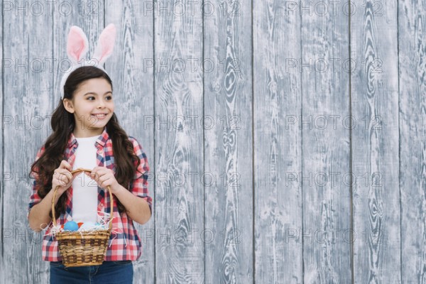 Portrait girl with bunny ears holding easter eggs basket looking away