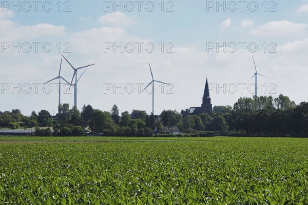 Wind turbines for power generation on the edge of the Garzweiler open-cast lignite mine, with a church tower behind, Rhenish lignite mining area, Germany
