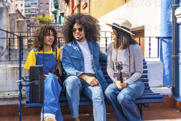 Three young content creators are recording a podcast outdoors, using a smartphone and microphone