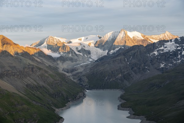 View at the summit of Mont de la Blana, alpenglow at sunset, view of a blue mountain lake, Lac des Dix reservoir, behind mountain peak Mont Blanc de Cheilon with glacier, Hérménence, Valais Alps, Valais, Switzerland