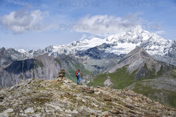 Female mountaineer on hiking trail with cairn, behind glaciated and snow-covered summit of the Großglockner, Wiener Höhenweg, Schober group, Hohe Tauern National Park, Carinthia, Austria