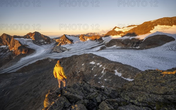 Mountaineers in front of a picturesque high mountain landscape at sunrise with alpenglow, glacier and rocky mountain peaks in the morning light, view at the Becher on mountain peaks Königshofspitz and Sonklarspitze and Schwarzwandspitz with glacier Übeltalferner, Stubai Alps, South Tyrol, Italy