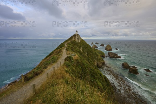 A lighthouse on narrow cliffs overlooking the sea under a cloudy sky, summer, Nugget Point lighthouse, Ahuriri Flat, Otago, South Island, New Zealand