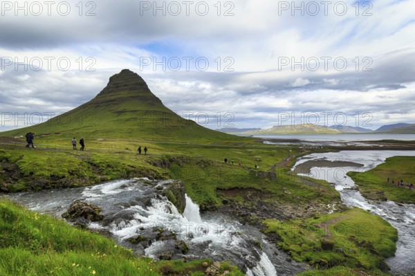 Kirkjufell mountain, film set, hikers, tourists at Kirkjufellfoss waterfall, Kirkjufellsa river, coastline at Grundarfjördur, Snæfellsnes peninsula, Vesturland, Iceland