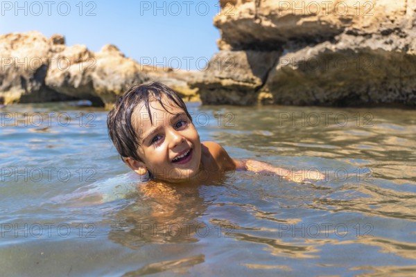 Young boy enjoying a refreshing swim in the ocean, surrounded by beautiful rock formations on a bright summer day