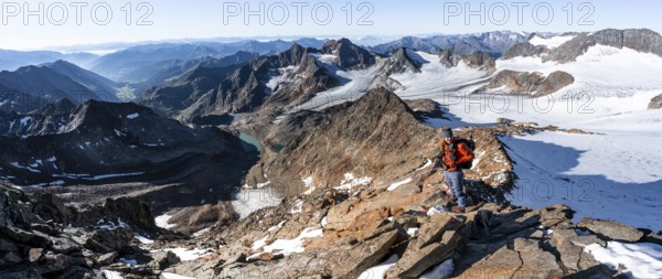 Mountaineer on a rocky ridge on the Wilder Freiger summit, behind him Signal summit and Becher summit with Becherhaus, picturesque high mountain landscape, view of Übeltalferner glacier and rocky mountain peaks Königshofspitz and Sonklarspitze, Stubai Alps, South Tyrol, Italy