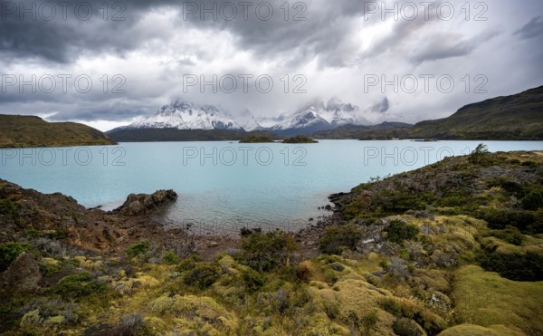 Cloudy mountain range Cuernos del Paine, shore of the blue lake Lago Pehoe in the evening light, dramatic sky, Torres del Paine National Park, Chile