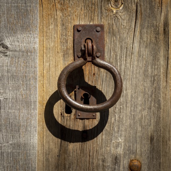 A weathered wooden door showcases an ornate metal knocker and an antique keyhole, reflecting the charm of traditional craftsmanship. The rustic textures add character and history