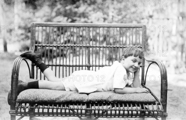 Young boy lying on a bench outdoors, 1920s, A boy lies smiling on a comfortable couch in the garden, Historical photo