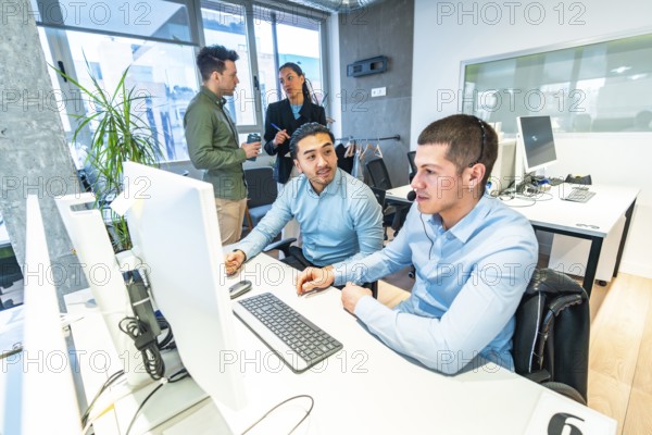 Two customer service representatives working on computer in a busy call center, assisted by their manager, with diverse colleagues standing in background
