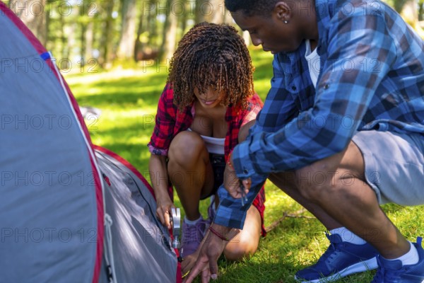 Young couple setting up a camping tent on a grassy campsite in a serene forest, embracing the joys of outdoor adventure and togetherness
