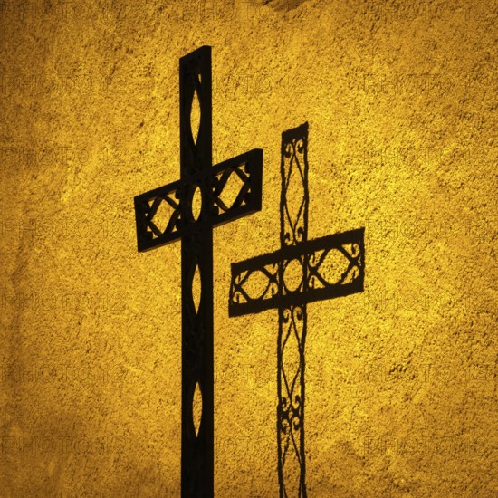 Shadow cast by one ornate cross on a textured wall at sunset illuminates the religious significance and artistry of faith. Auvergne. France