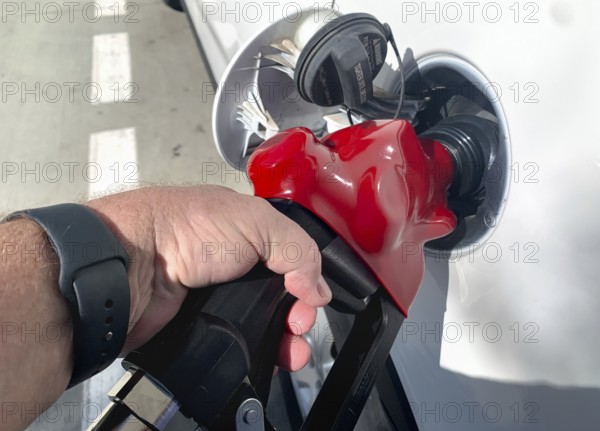 Male hand holding gas pump nozzle pumping gas into vehicle