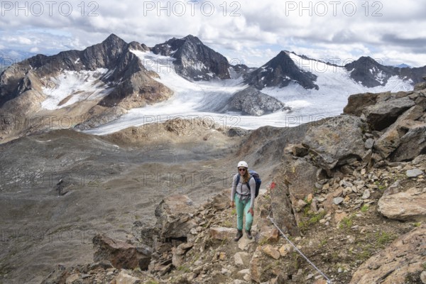 Mountaineer with helmet on a rope-insured path, in high mountain landscape, ascent to the Becher, view of the mountain peaks Königshofspitz and Hofmannspitze with glacier of the Übeltalferner, Stubai Alps, South Tyrol, Italy