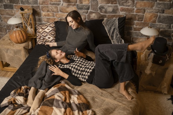 Two friends relax on a cozy bed, enjoying each others company. The warm atmosphere features autumn decorations, including a pumpkin and soft textiles, perfect for a chill evening together