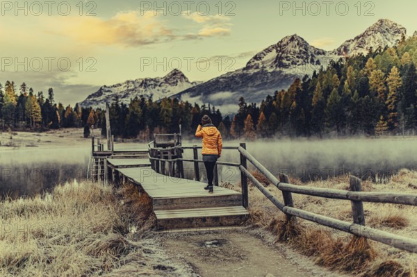 Young woman at Lake Staz near Sankt Moritz in the Engadine in Switzerland. Morning atmosphere with fog in autumn. Reflection of water