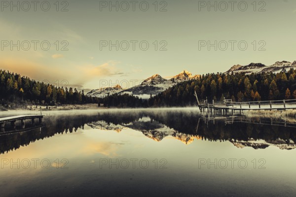 Lake Staz near Sankt Moritz in the Engadin in Switzerland. Morning atmosphere with fog in autumn. Water reflection and snow-covered mountains in the background