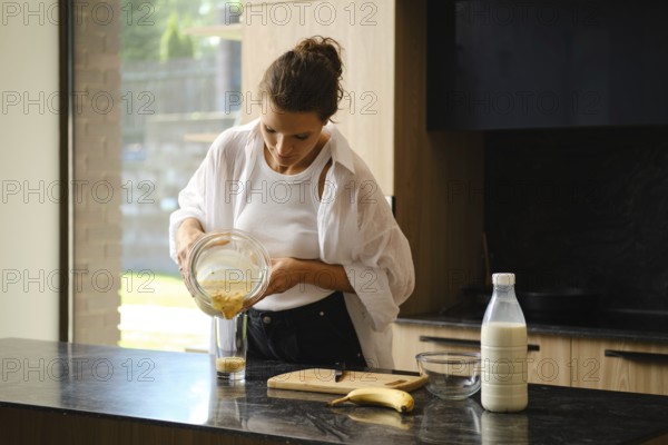 A person blends banana and sea buckthorn in a cozy kitchen. Ingredients are prepared on the counter, with natural light highlighting the freshness of the smoothie-making process