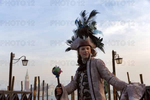 Tourist at the carnival, Venetian costume with hat, disguised man, boat dock at St Mark's Square, in the background church San Giorgio Maggiore, Venice, Italy