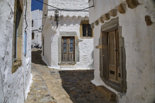 Narrow, stone-paved alley with white historic buildings and wooden windows on a sunny day, Mantomata Stones, Chora, UNESCO World Heritage Site 1999, Patmos, Dodecanese, Greek Islands, Greece