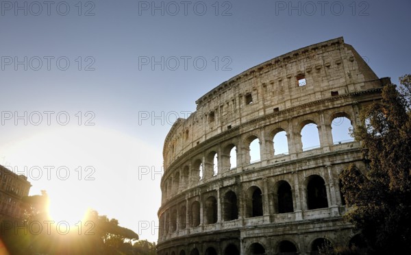 The Colosseum stands majestically against a setting sun, highlighting its ancient stone structure and arched entrances while visitors admire its grandeur in Rome. Italy