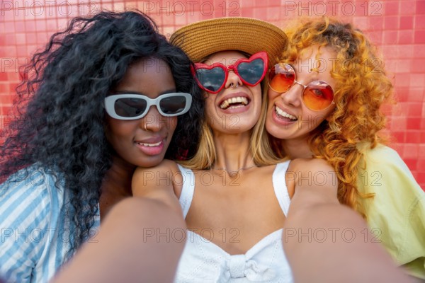 Three cheerful women with sunglasses are taking a selfie, smiling and enjoying their time together against a vibrant backdrop