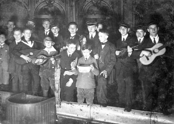 Boys in school uniform giving a performance, 1930s, Young men with guitars and mandolins, one drinking from a bowl, historical photo