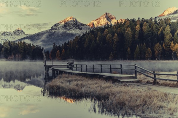 Lake Staz near Sankt Moritz in the Engadin in Switzerland. Morning atmosphere with fog in autumn. Water reflection and snow-covered mountains in the background