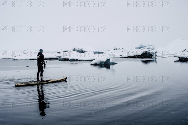 Man stand up paddling, snowfall, glacial lake Jökulsarlon at Vatnajökull, Iceland* Man stand up paddling on glacial lake Jokulsarlonat Vatnajokul, snowfall, Iceland