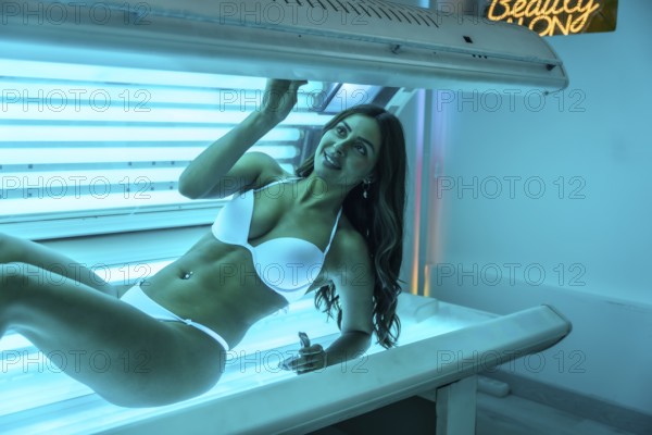 Young woman smiling while enjoying the warmth of a tanning bed, soaking up uv light for a beautifully even tan indoors