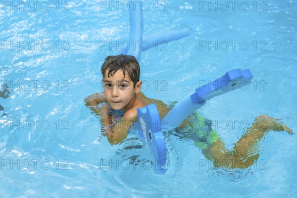 Young boy enjoying summer days, playing with a blue floating toy in a refreshing blue pool under the warm sun, radiating joy