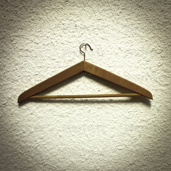 A wooden clothes hanger is resting on a textured wall, showcasing its natural finish and design. The scene emphasizes minimalism, highlighting practicality in home organization