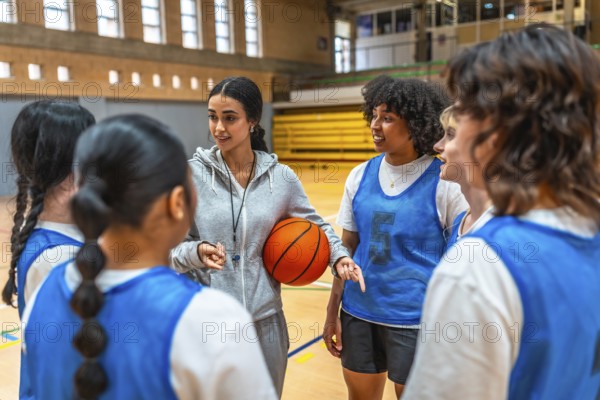 Female basketball coach holding ball and explaining game strategy to her team during training in a gymnasium