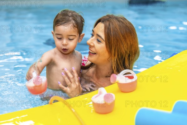 Mother and baby daughter enjoying playful moments with colorful toys in a swimming pool, creating joyful memories during summer vacation