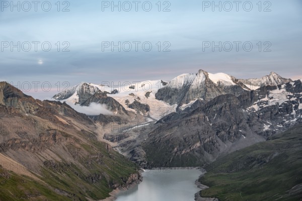 Mountain landscape with turquoise blue reservoir Lac des Dix and summit Mont Blanc de Cheilon, moon above mountain peaks at sunset, Hérménence, Valais Alps, Valais, Switzerland