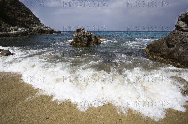 Energetic waves meet rocks on the sandy beach under a slightly cloudy sky, Ricadi, Capo Vaticano