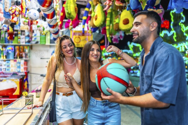Happy friends enjoying time at an amusement park, playing a basketball game and celebrating their victory with a fun prize
