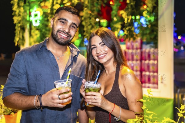 Young couple smiling and holding cocktails at a night market, enjoying the vibrant atmosphere and refreshing drinks